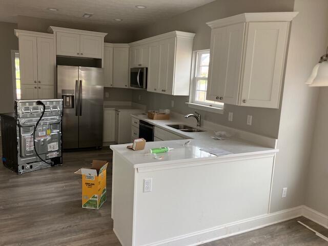 kitchen with dark wood-type flooring, white cabinets, kitchen peninsula, sink, and appliances with stainless steel finishes