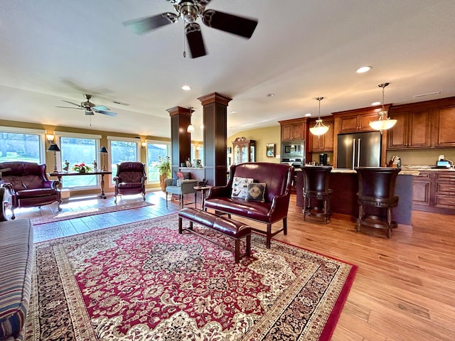 living room with light hardwood / wood-style flooring, ceiling fan, and ornate columns