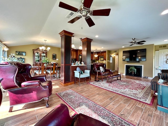 living room featuring ceiling fan with notable chandelier, light hardwood / wood-style flooring, decorative columns, and lofted ceiling