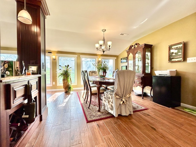 dining room with a notable chandelier, light hardwood / wood-style floors, and vaulted ceiling