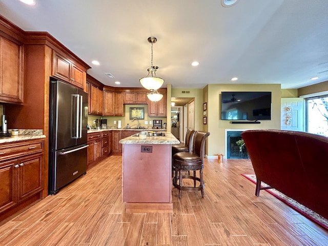 kitchen featuring light stone countertops, high end refrigerator, hanging light fixtures, a center island, and a breakfast bar