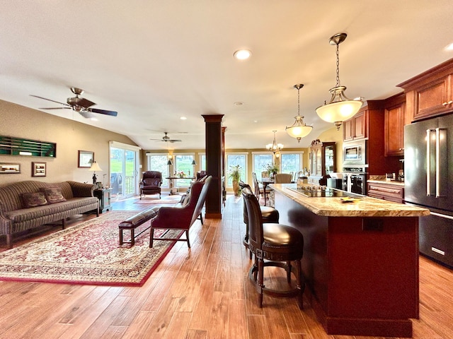 kitchen with a kitchen bar, ceiling fan with notable chandelier, stainless steel appliances, light hardwood / wood-style flooring, and pendant lighting