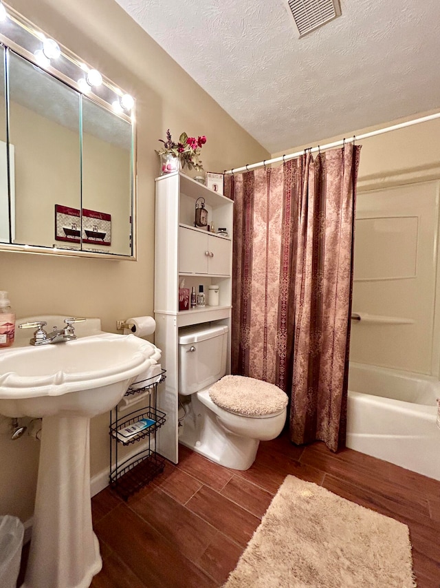 bathroom with a textured ceiling, hardwood / wood-style flooring, toilet, and shower / bath combo with shower curtain