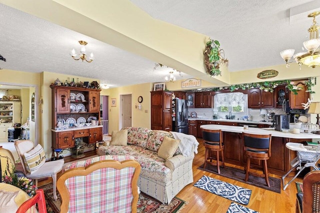 living room featuring a textured ceiling, sink, light wood-type flooring, and a chandelier