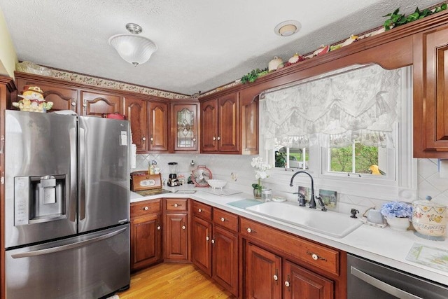 kitchen with appliances with stainless steel finishes, a textured ceiling, sink, tasteful backsplash, and light wood-type flooring