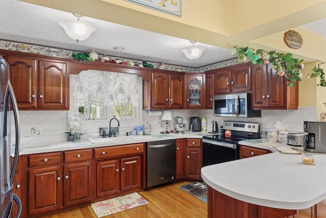 kitchen with kitchen peninsula, backsplash, stainless steel appliances, sink, and light wood-type flooring