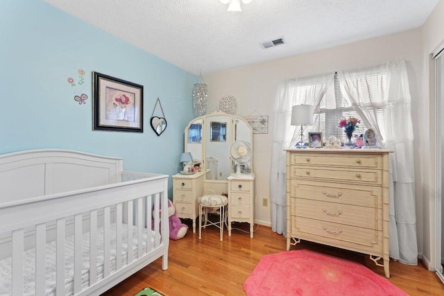 bedroom with light hardwood / wood-style flooring, a crib, and a textured ceiling