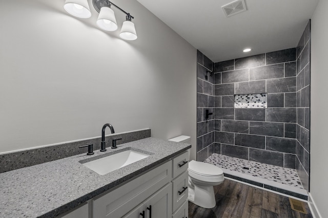 bathroom with toilet, vanity, hardwood / wood-style floors, and a tile shower