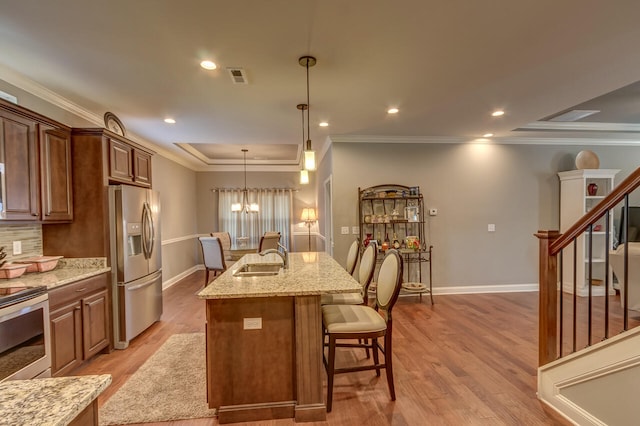 kitchen featuring light stone counters, appliances with stainless steel finishes, light hardwood / wood-style flooring, an island with sink, and an inviting chandelier