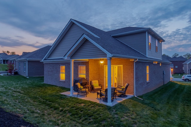 back house at dusk with a patio and a lawn