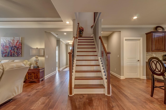 stairs featuring hardwood / wood-style flooring, ornamental molding, and a raised ceiling