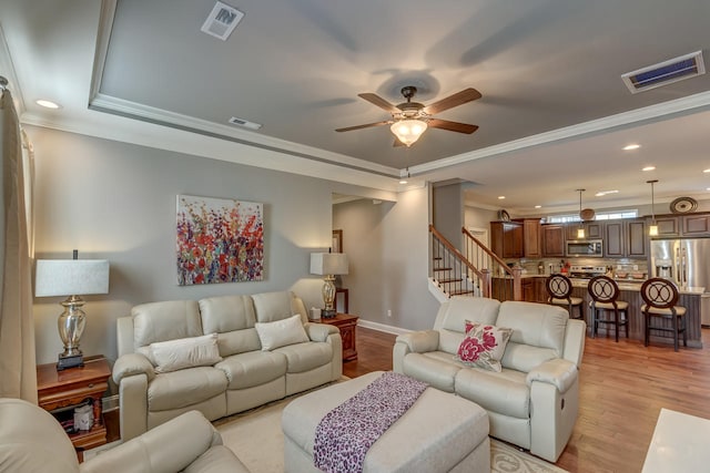 living room featuring ornamental molding, light hardwood / wood-style flooring, ceiling fan, and a tray ceiling