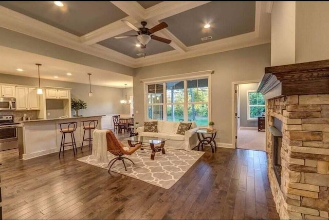 living area with beamed ceiling, ceiling fan, a stone fireplace, coffered ceiling, and dark hardwood / wood-style flooring