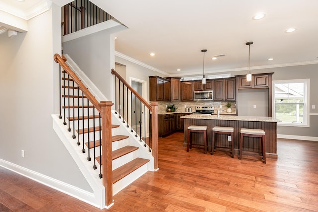 kitchen featuring appliances with stainless steel finishes, light hardwood / wood-style floors, backsplash, hanging light fixtures, and a kitchen island with sink