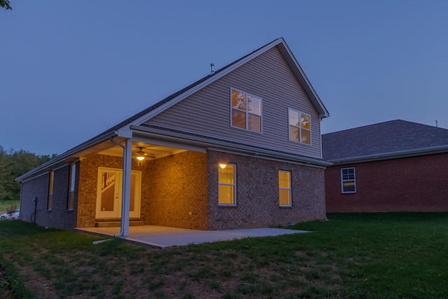 back house at dusk featuring a patio and a lawn