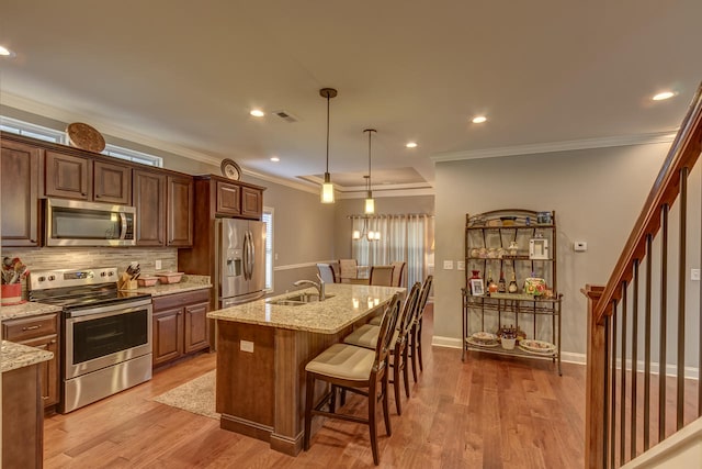 kitchen with a kitchen breakfast bar, hanging light fixtures, light wood-type flooring, stainless steel appliances, and light stone counters