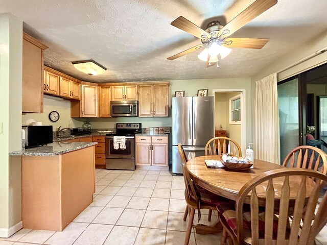 kitchen with light stone counters, appliances with stainless steel finishes, ceiling fan, sink, and light tile flooring