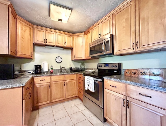 kitchen with light tile flooring, stainless steel appliances, sink, dark stone counters, and a textured ceiling