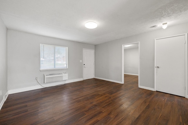 spare room with a wall mounted air conditioner, a textured ceiling, and dark hardwood / wood-style floors