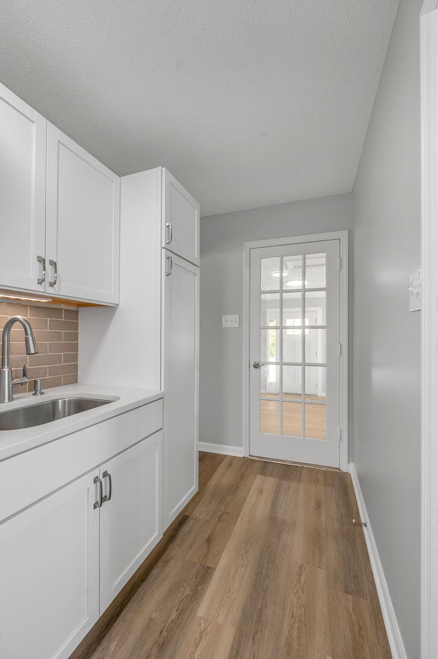 kitchen with white cabinetry, sink, tasteful backsplash, light hardwood / wood-style floors, and a textured ceiling