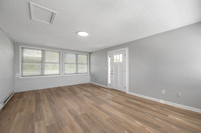 empty room with hardwood / wood-style flooring, a baseboard radiator, brick wall, and a textured ceiling