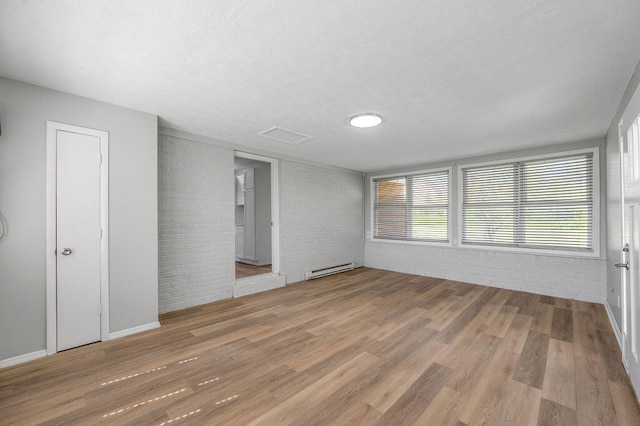 spare room with brick wall, a baseboard heating unit, and hardwood / wood-style floors