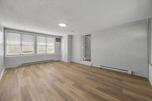 unfurnished room featuring hardwood / wood-style floors, brick wall, a baseboard radiator, and a textured ceiling