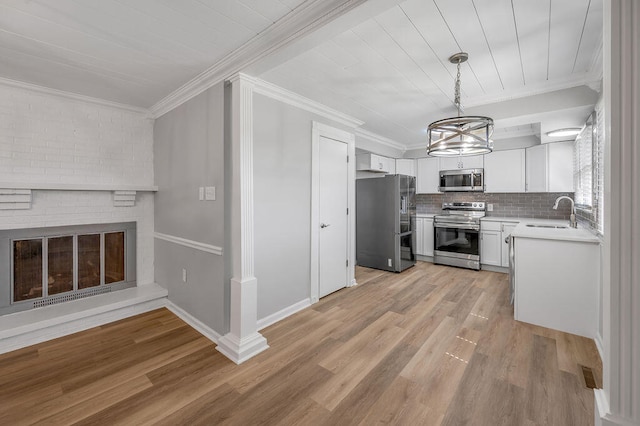 kitchen with decorative light fixtures, appliances with stainless steel finishes, light hardwood / wood-style flooring, white cabinetry, and a fireplace