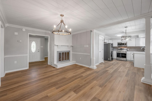 unfurnished living room with a fireplace, ornamental molding, an inviting chandelier, sink, and hardwood / wood-style flooring