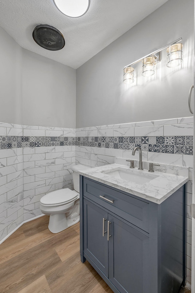 bathroom with wood-type flooring, vanity, tile walls, toilet, and a textured ceiling