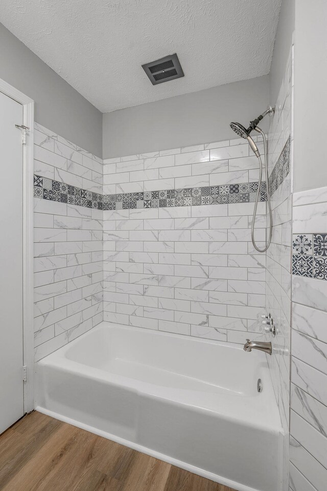 bathroom featuring a textured ceiling, hardwood / wood-style floors, and tiled shower / bath