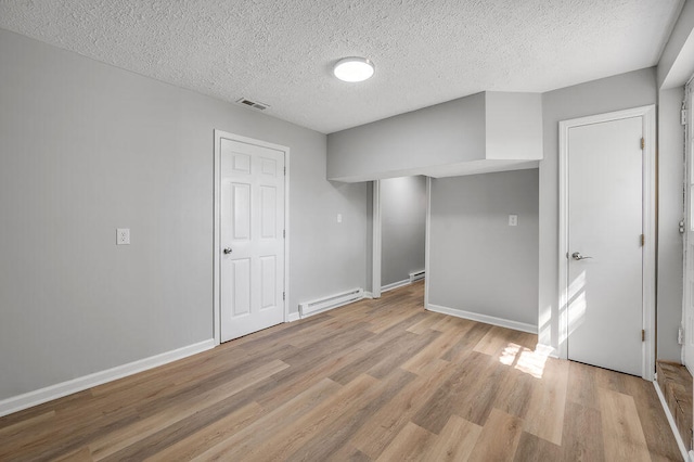 empty room with light hardwood / wood-style flooring, a textured ceiling, and a baseboard heating unit