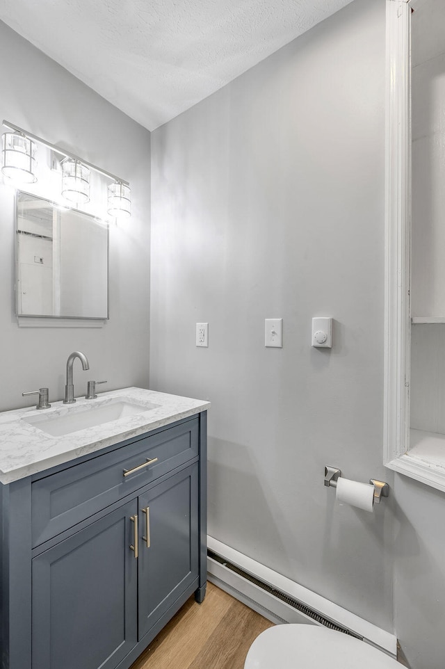 bathroom featuring a textured ceiling, hardwood / wood-style floors, toilet, vanity, and baseboard heating