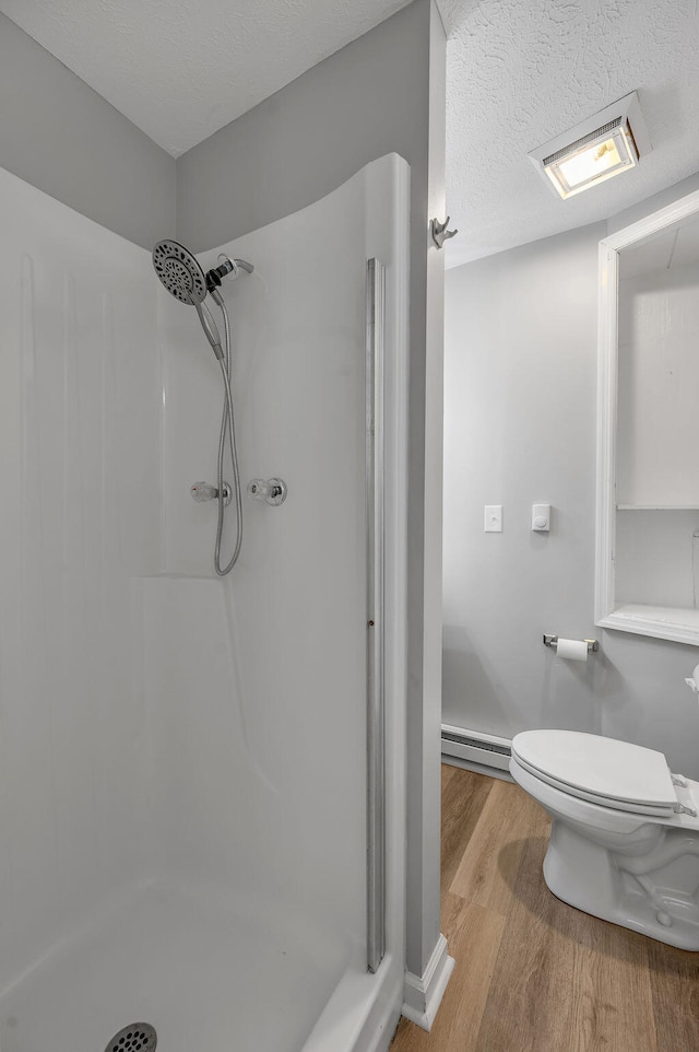 bathroom featuring a baseboard heating unit, a shower, toilet, wood-type flooring, and a textured ceiling