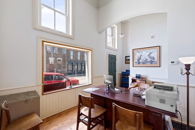 home office with a healthy amount of sunlight, wood-type flooring, and a high ceiling