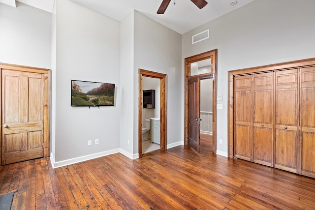 unfurnished bedroom with hardwood / wood-style floors, ceiling fan, ensuite bathroom, and a towering ceiling