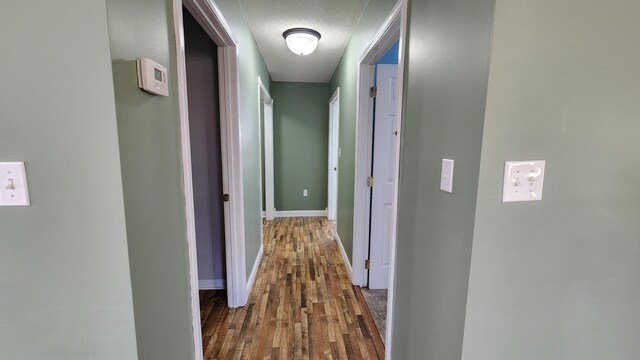 corridor with a textured ceiling and hardwood / wood-style floors