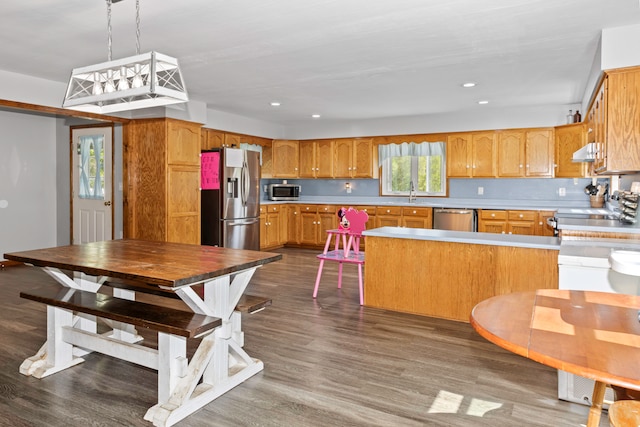 kitchen with hanging light fixtures, stainless steel appliances, dark wood-type flooring, and range hood