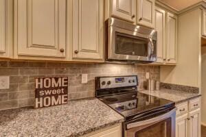 kitchen with electric range, backsplash, light stone countertops, and cream cabinets