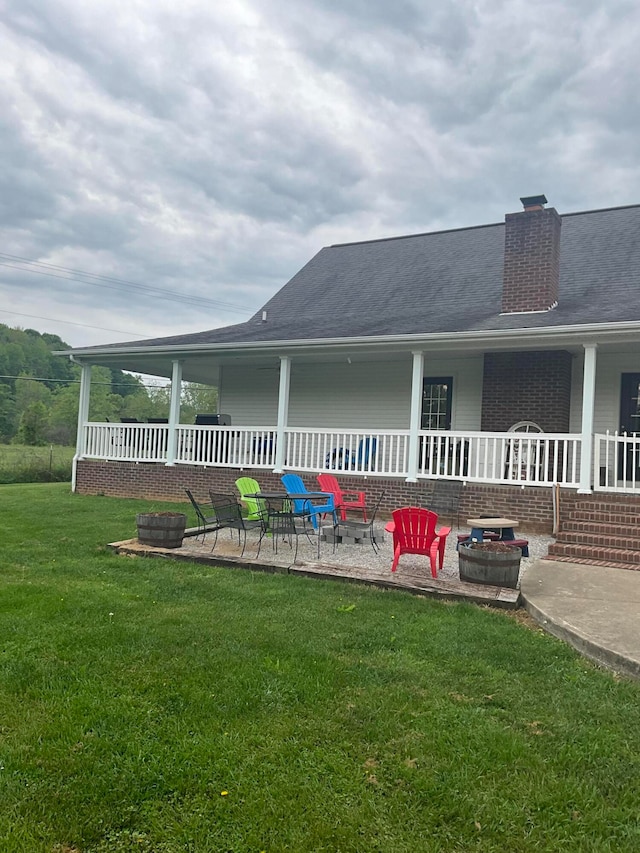 back of house featuring a yard, covered porch, an outdoor fire pit, and a patio