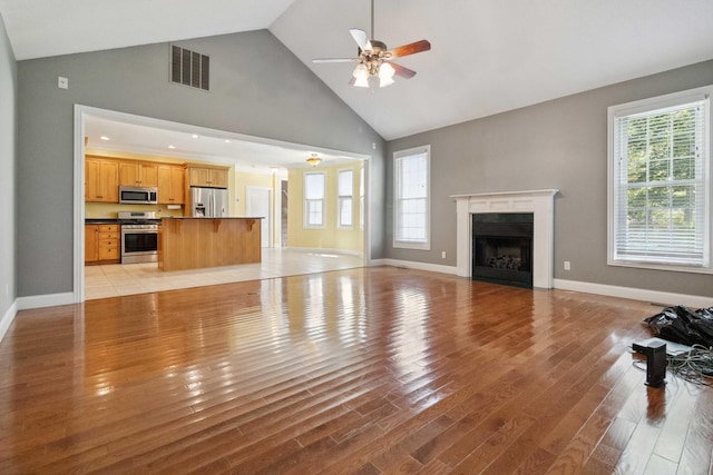 unfurnished living room featuring high vaulted ceiling, a healthy amount of sunlight, light hardwood / wood-style flooring, and ceiling fan