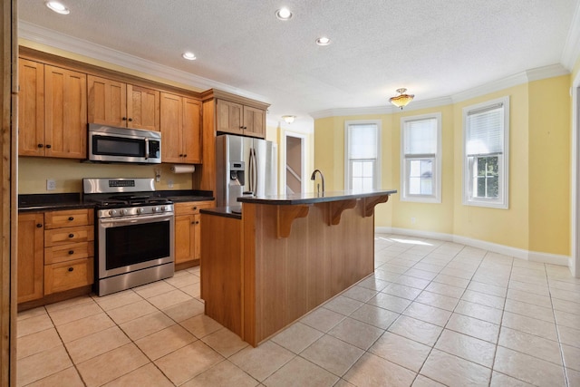 kitchen with crown molding, appliances with stainless steel finishes, light tile patterned floors, and a kitchen island with sink