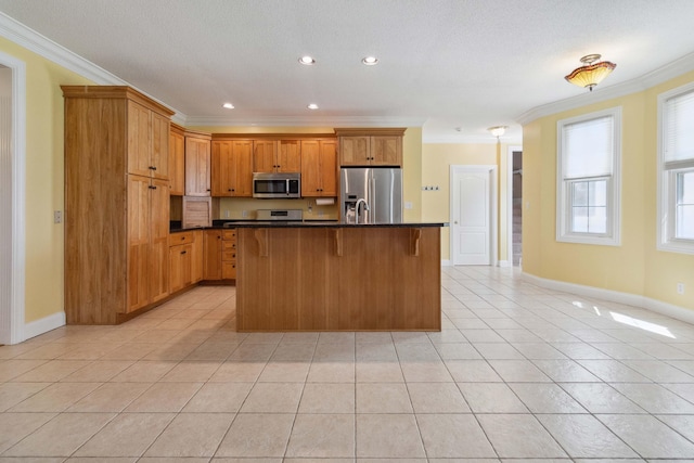 kitchen featuring light tile patterned floors, appliances with stainless steel finishes, an island with sink, crown molding, and a breakfast bar