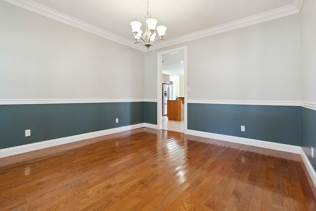 spare room featuring ornamental molding, wood-type flooring, and an inviting chandelier