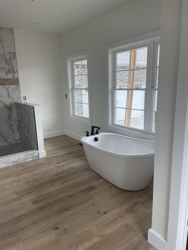 bathroom with a marble finish shower, a soaking tub, wood finished floors, and a wealth of natural light