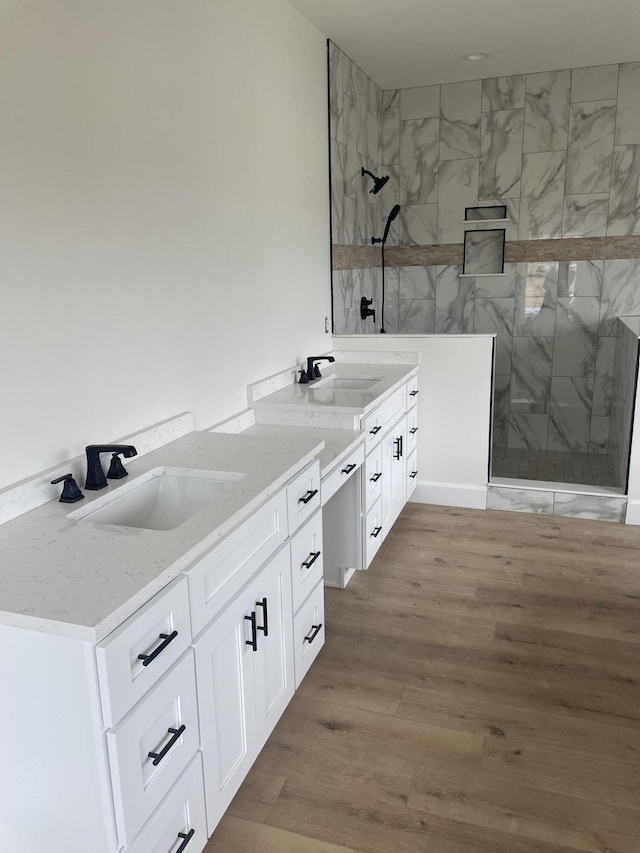 full bathroom with a tile shower, vanity, and wood finished floors