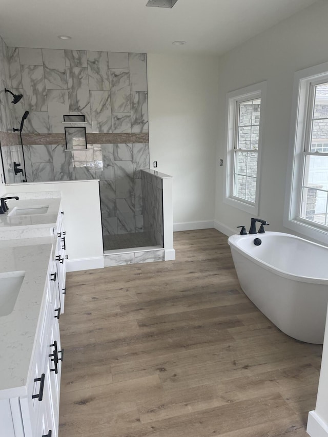 bathroom featuring wood finished floors, double vanity, a freestanding tub, and walk in shower