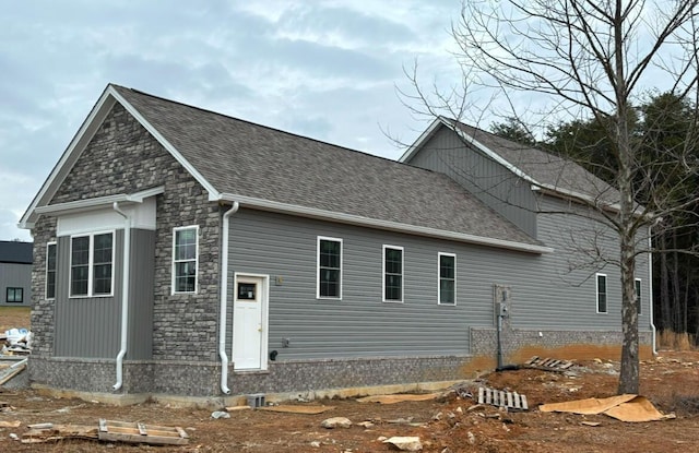 rear view of house featuring stone siding and roof with shingles