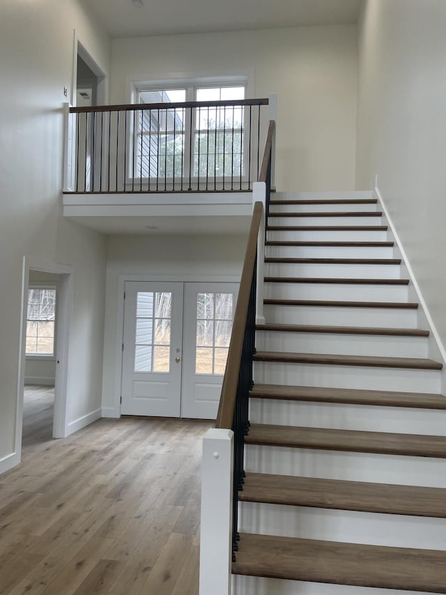 stairway with french doors, baseboards, a high ceiling, and wood finished floors