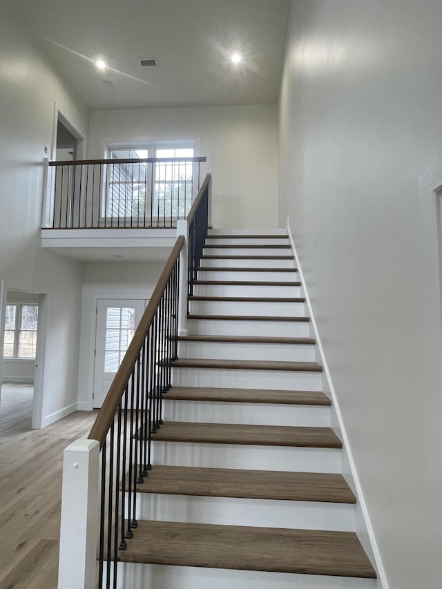 staircase with a high ceiling, recessed lighting, wood finished floors, and baseboards